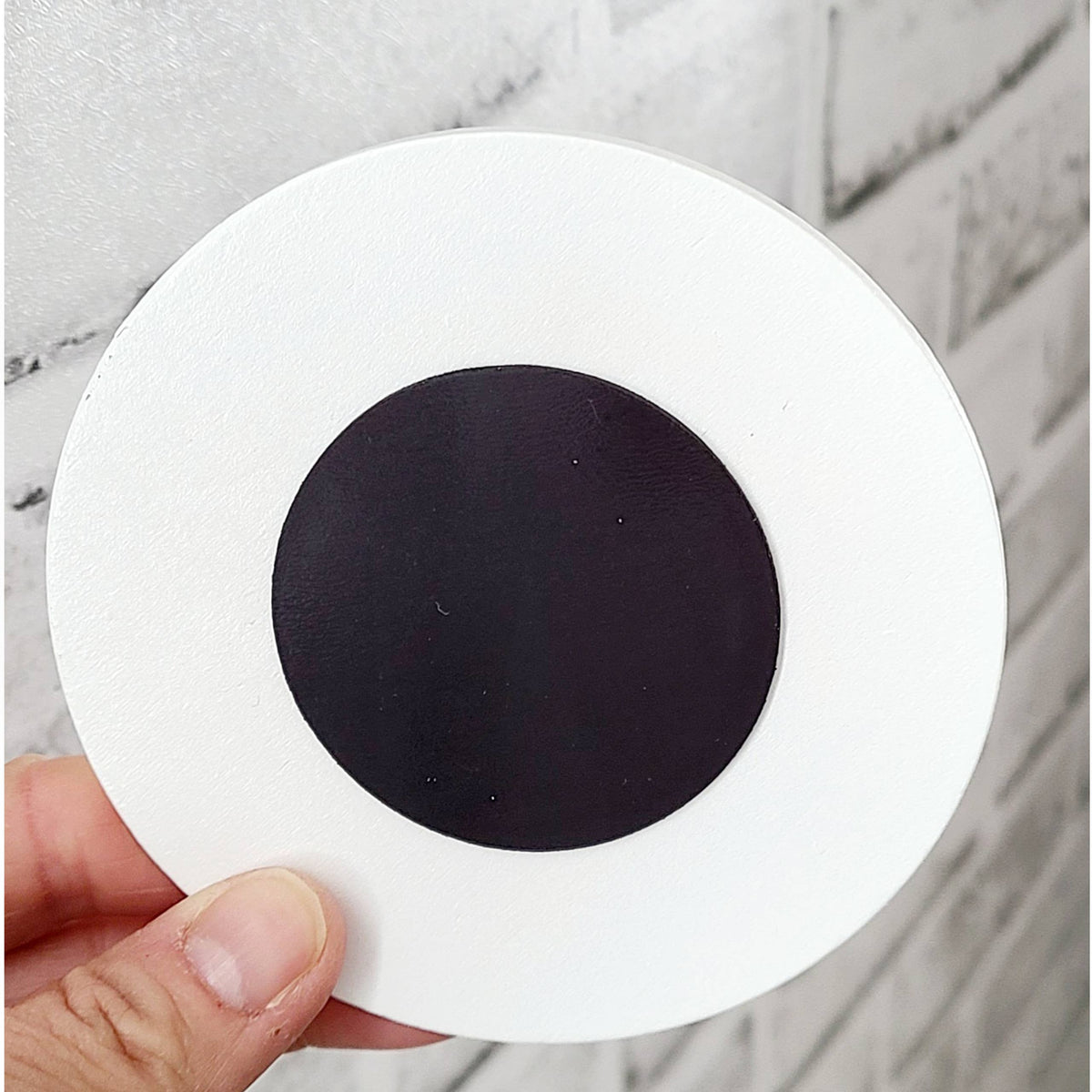 Round white object with a black center held by a hand on a marble surface