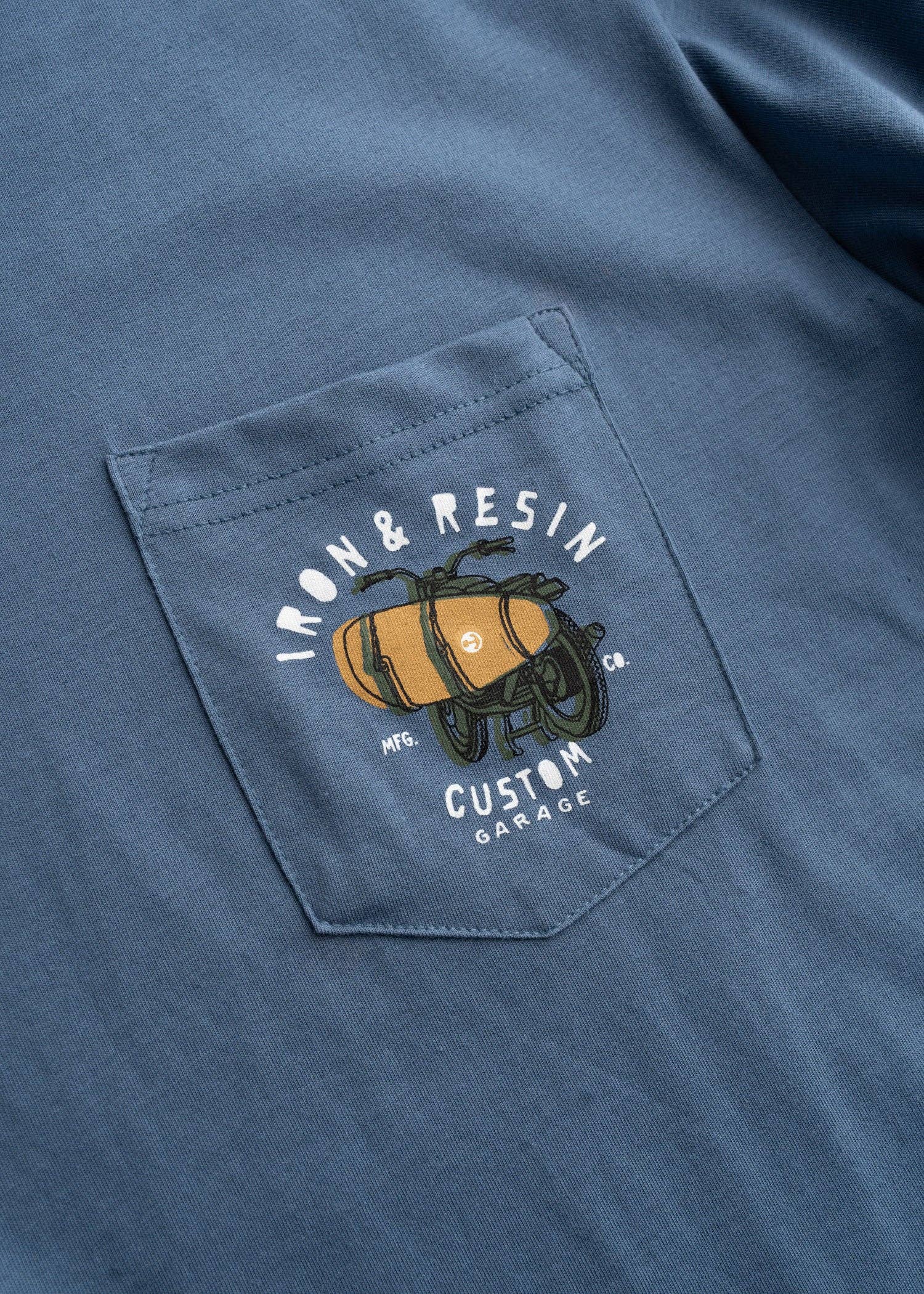 Blue shirt with a pocket featuring an embroidered design of a barrel and text.