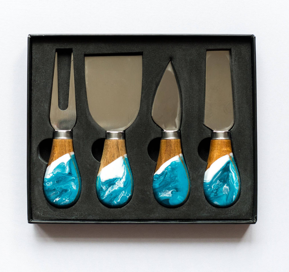 Set of four cheese knives with wooden handles featuring blue and white designs, in a black box.