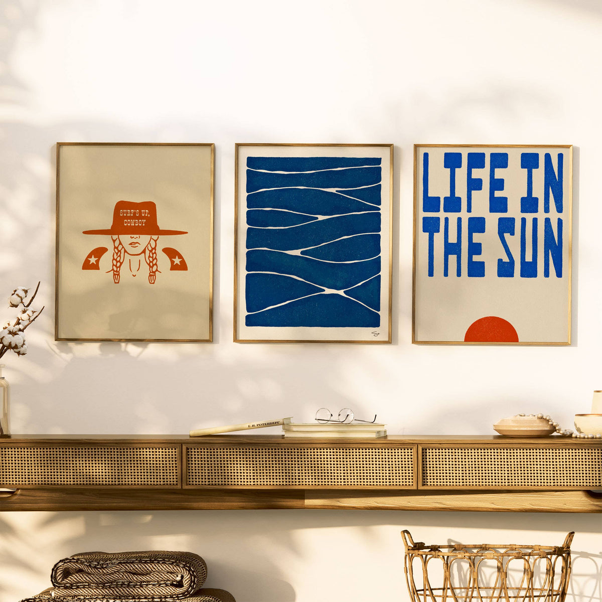 Three framed artworks on a wall above a shelf with decorative items.