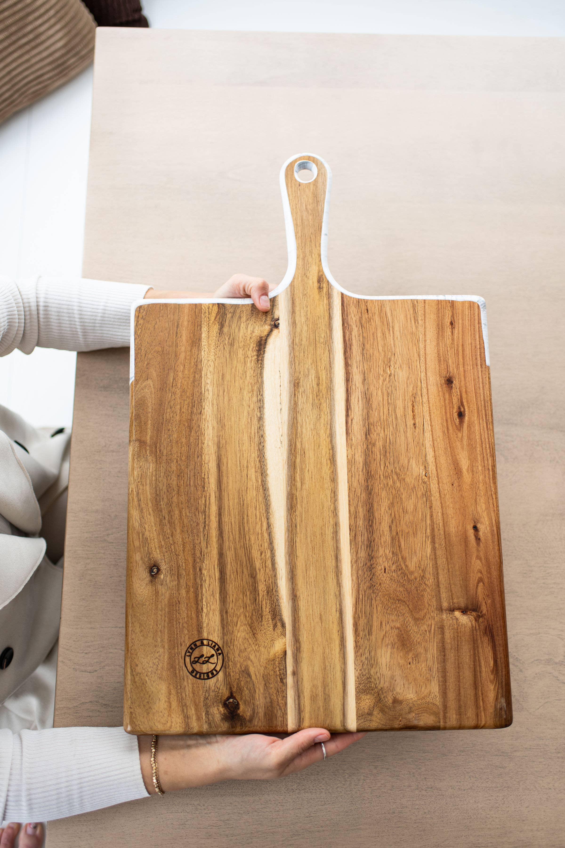 Wooden cutting board with a handle held by a person on a light-colored surface