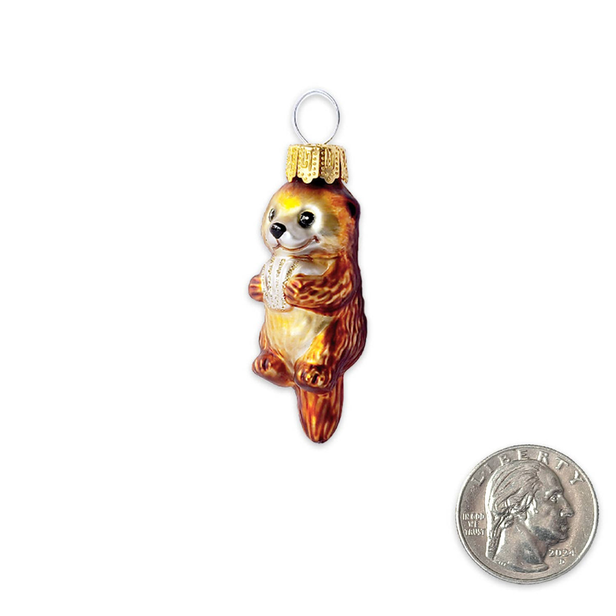 A small hand-painted glass ornament shaped like a brown and cream otter holding a white sweater, shown next to a US quarter for scale on a white background.