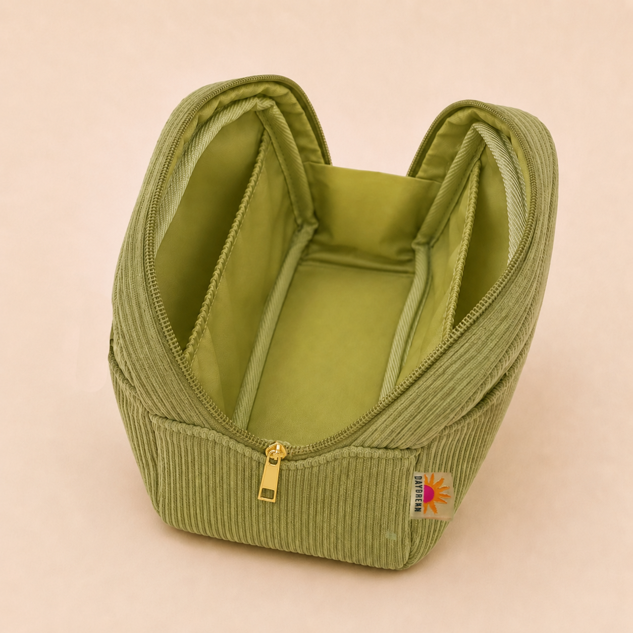 An olive green corduroy cosmetic pouch with a gold zipper and a small colorful brand tag, shown open on a solid light beige background.