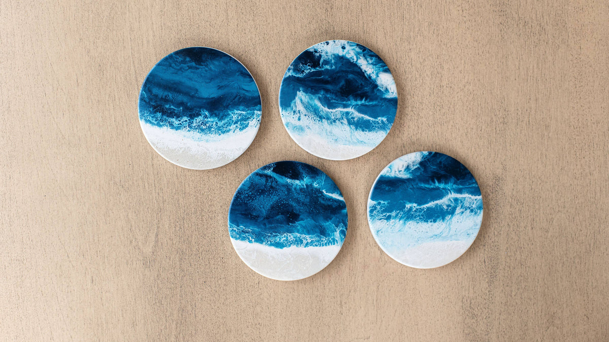 Four round coasters with a blue and white ocean wave pattern, arranged on a light beige textured background.