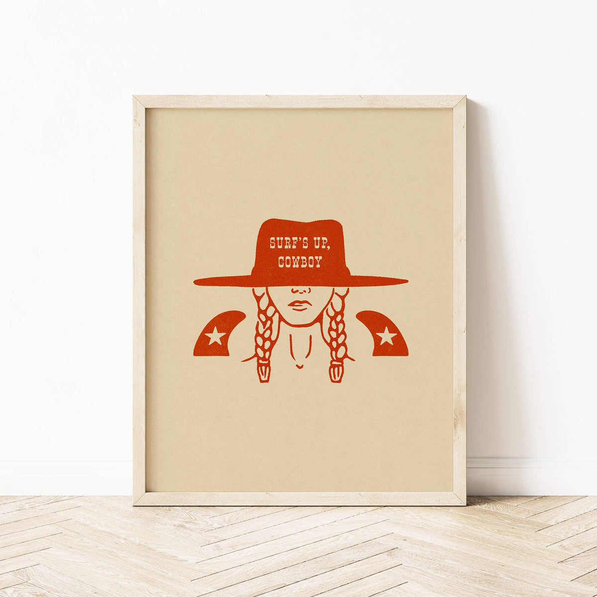 Framed artwork with a red illustration of a person wearing a cowboy hat and buns on a beige background.