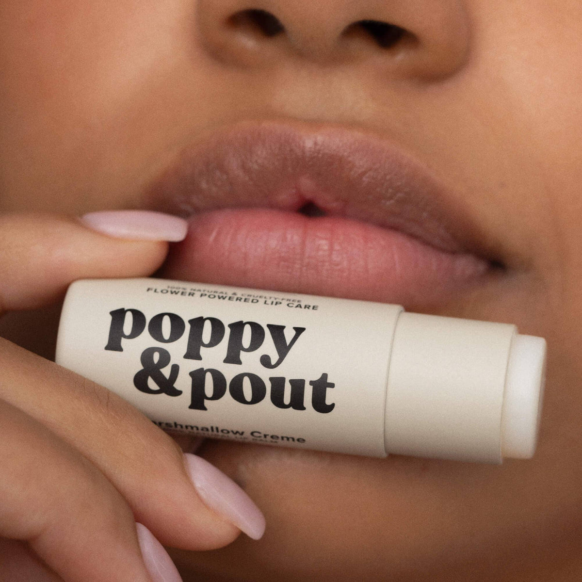 Lip balm stick with 'poppy & pout' branding held by a person's hand.