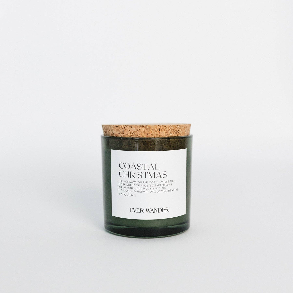 A dark green glass jar candle with a natural cork lid and a white label reading 'COASTAL CHRISTMAS' and 'EVER WANDER', centered on a clean white background.