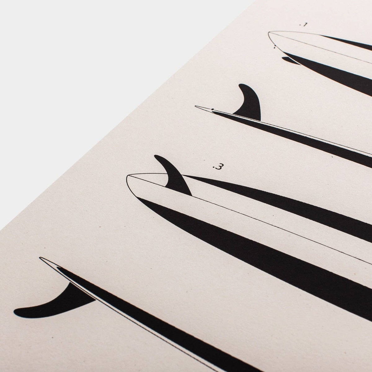 A minimalist art print featuring black surfboard fin silhouettes on a warm off-white paper background, photographed at an angle against a clean white backdrop.