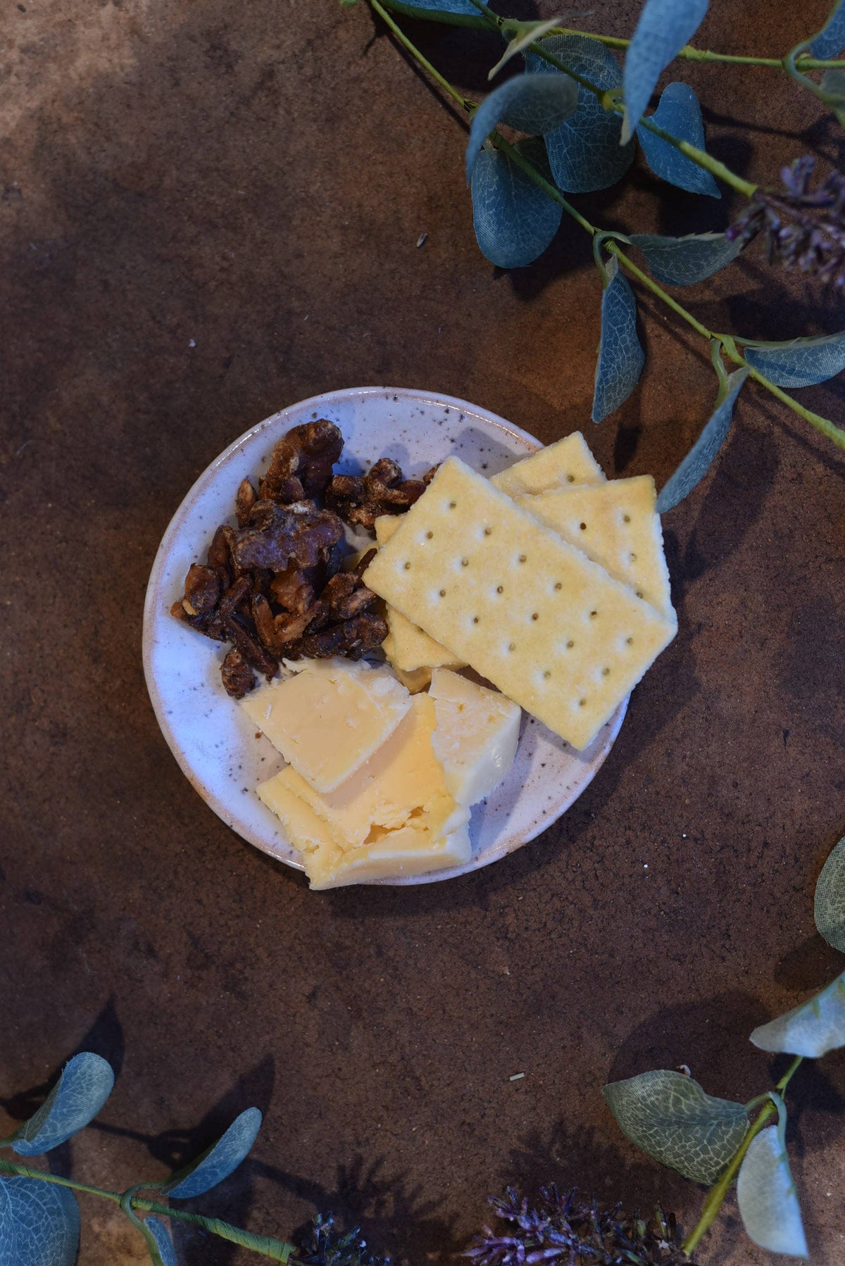 Small plate with crackers, cheese, and dried fruit on a wooden surface with greenery.