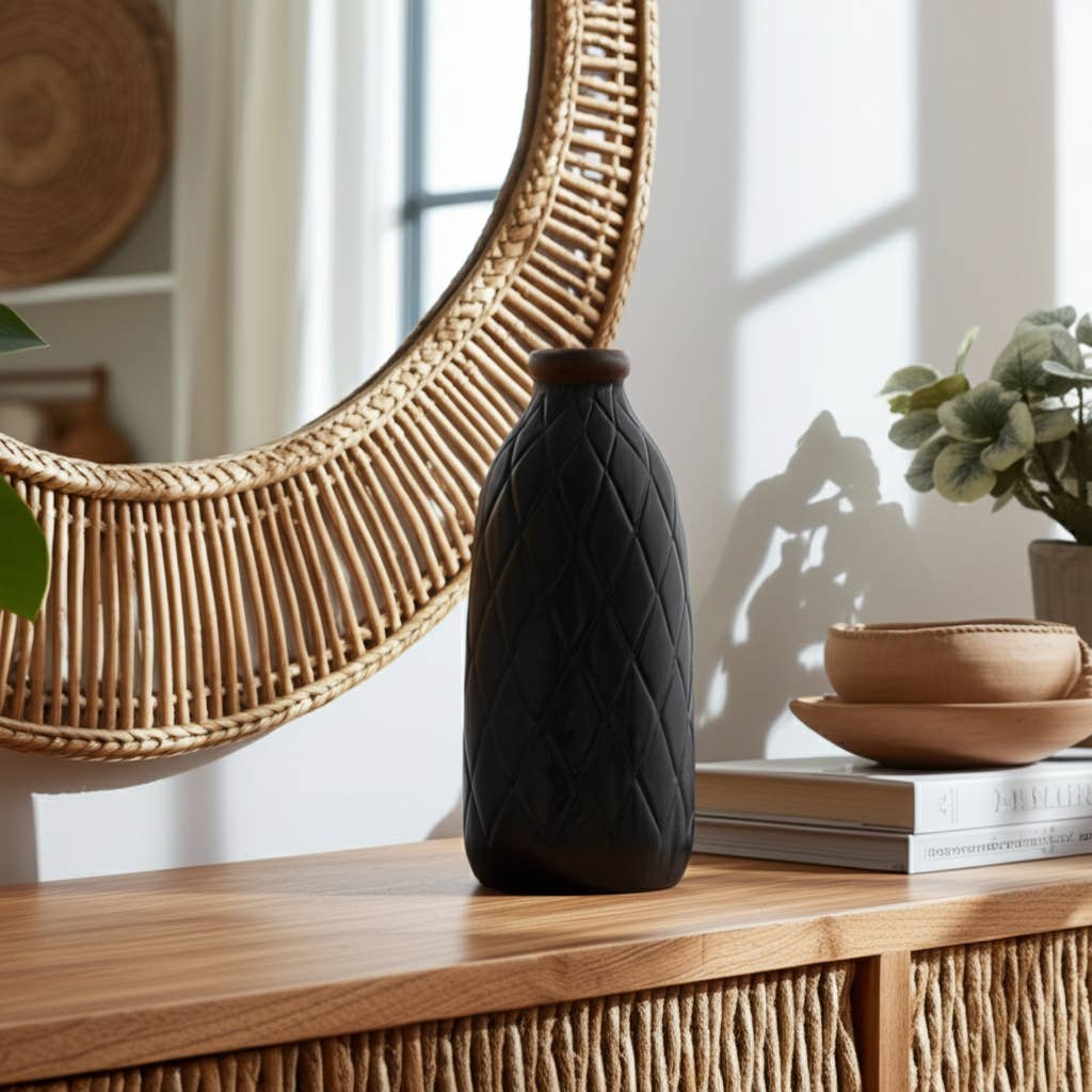 Black textured vase on a wooden surface with a woven mirror and books in the background