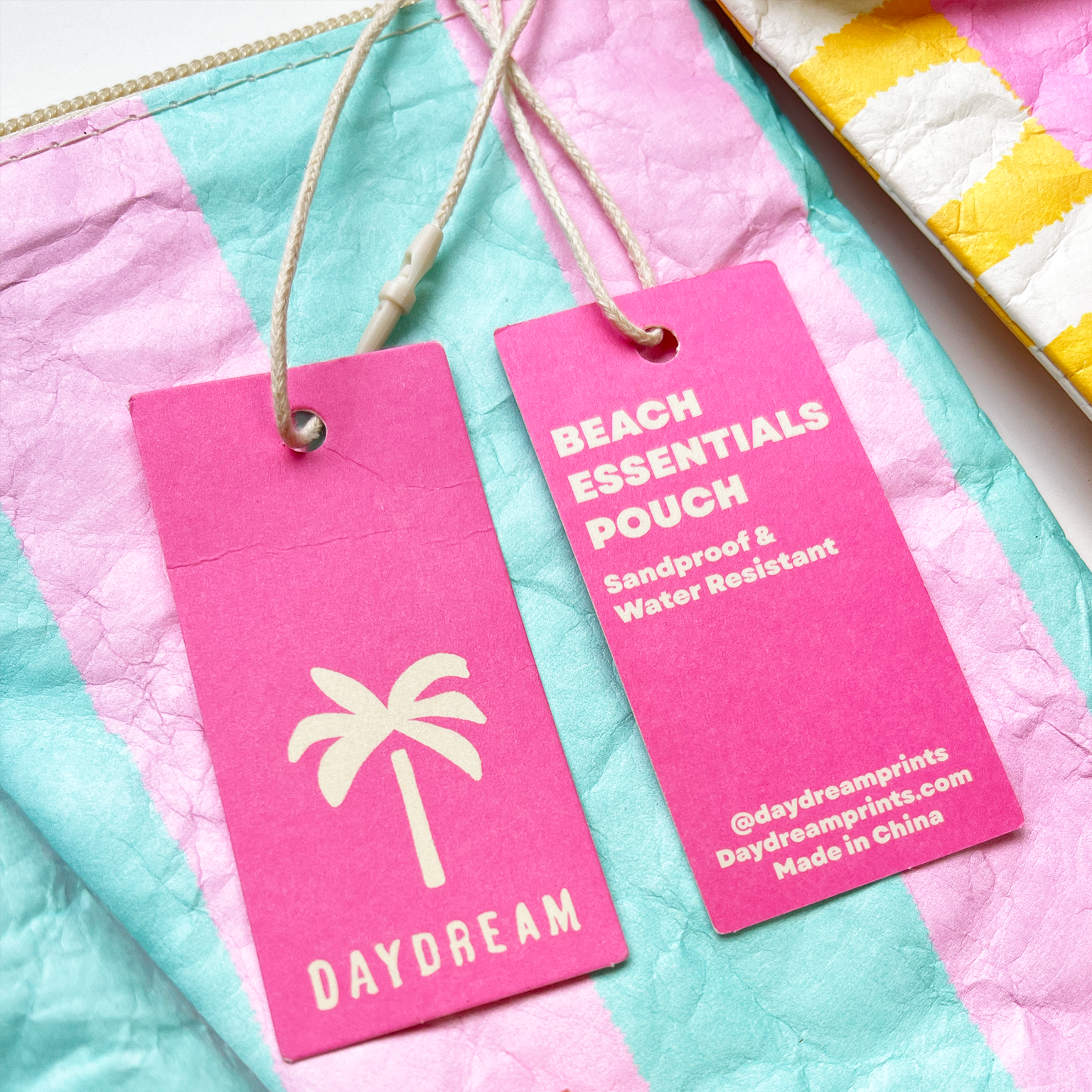 Pink 'Beach Essentials Pouch' tag with palm tree design on a colorful fabric background