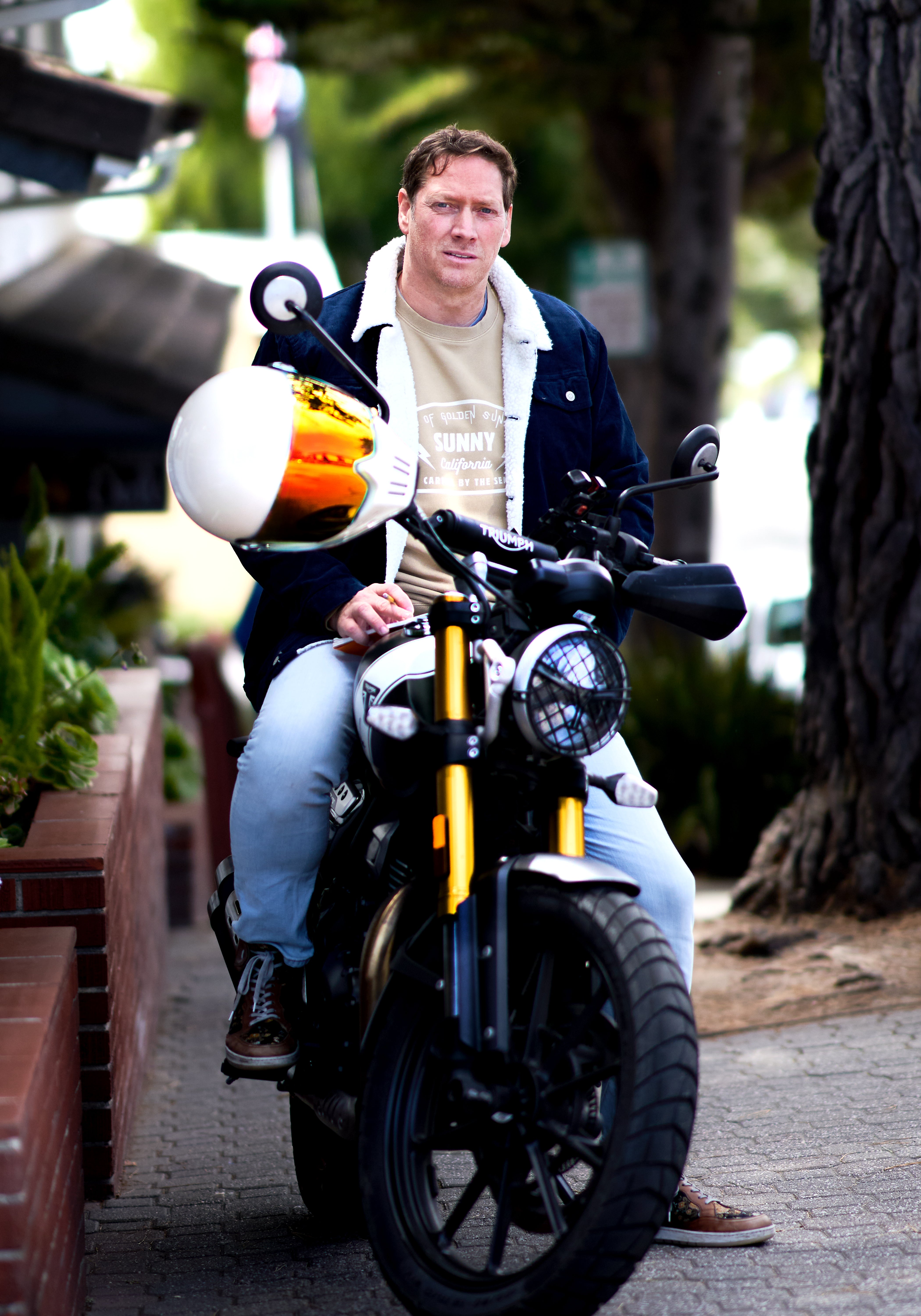 Man sitting on a motorcycle with a helmet on his lap in an urban setting
