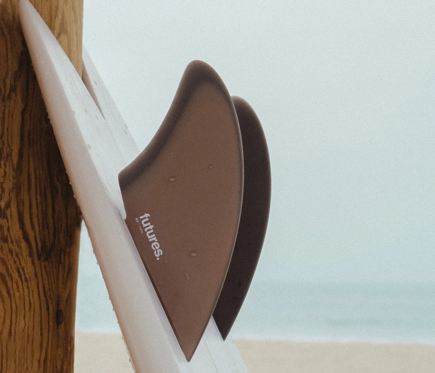 Futures K2 Fiberglass Keel Fin Set on a white surfboard with a beach and ocean background.