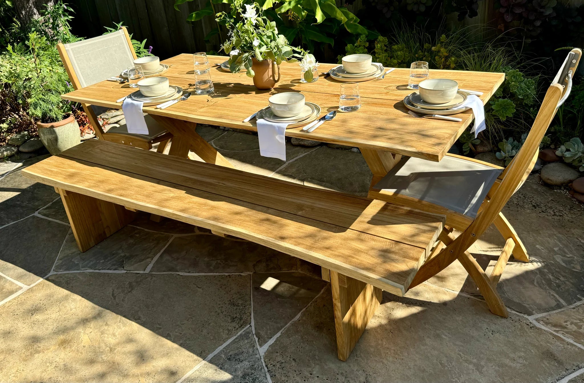 Wooden outdoor dining table with chairs and benches on a stone patio