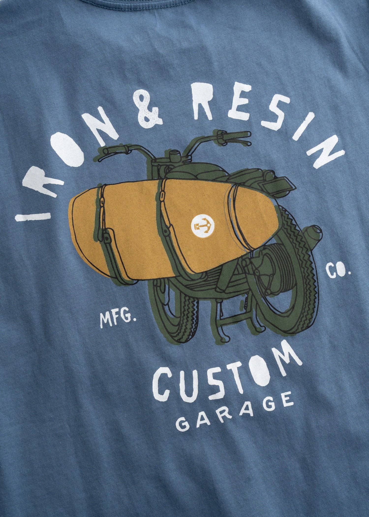 Blue t-shirt with a graphic of a motorcycle and saddlebags, featuring the text 'Iron & Resin Custom Garage'.