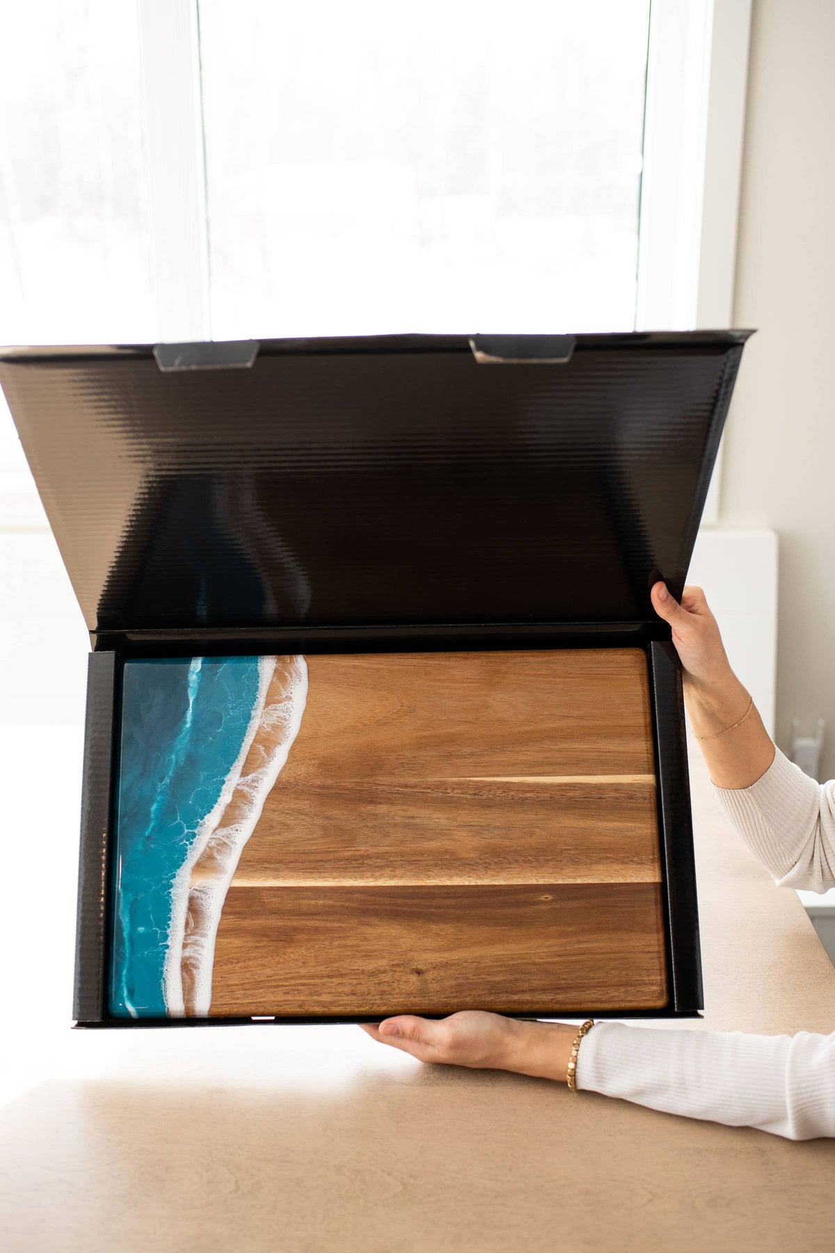 Person holding a large open box with a wooden design on a light-colored surface.