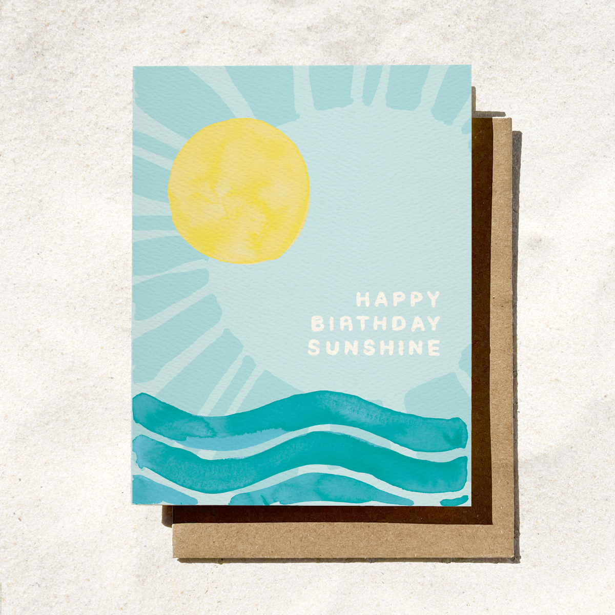 Greeting card with sun and water design and 'Happy Birthday Sunshine' text on a textured surface.