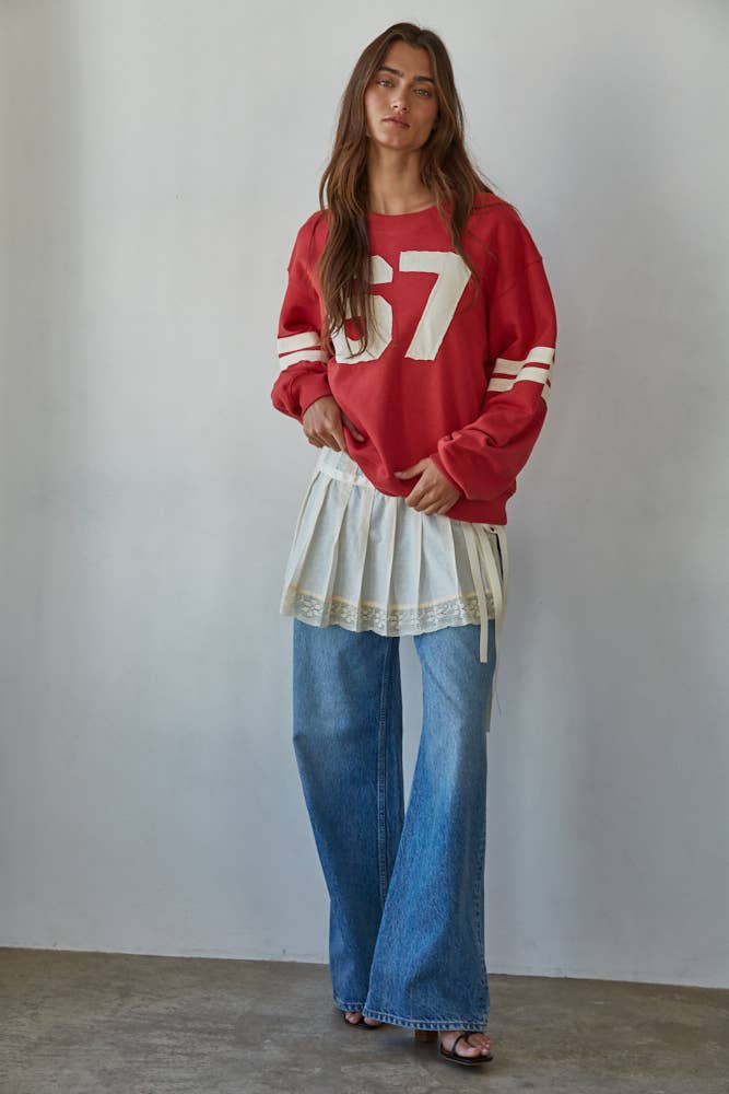 Woman wearing a red sweater with a number, white skirt, and blue jeans against a plain background