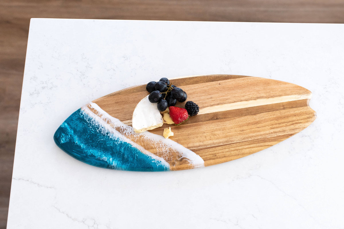 Wooden surfboard-shaped cutting board with a decorative edge on a white surface.