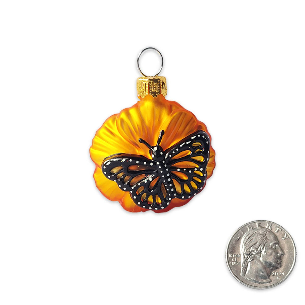 A glass Christmas ornament shaped like a flower with a monarch butterfly on it, shown on a white background with a US quarter coin for scale.