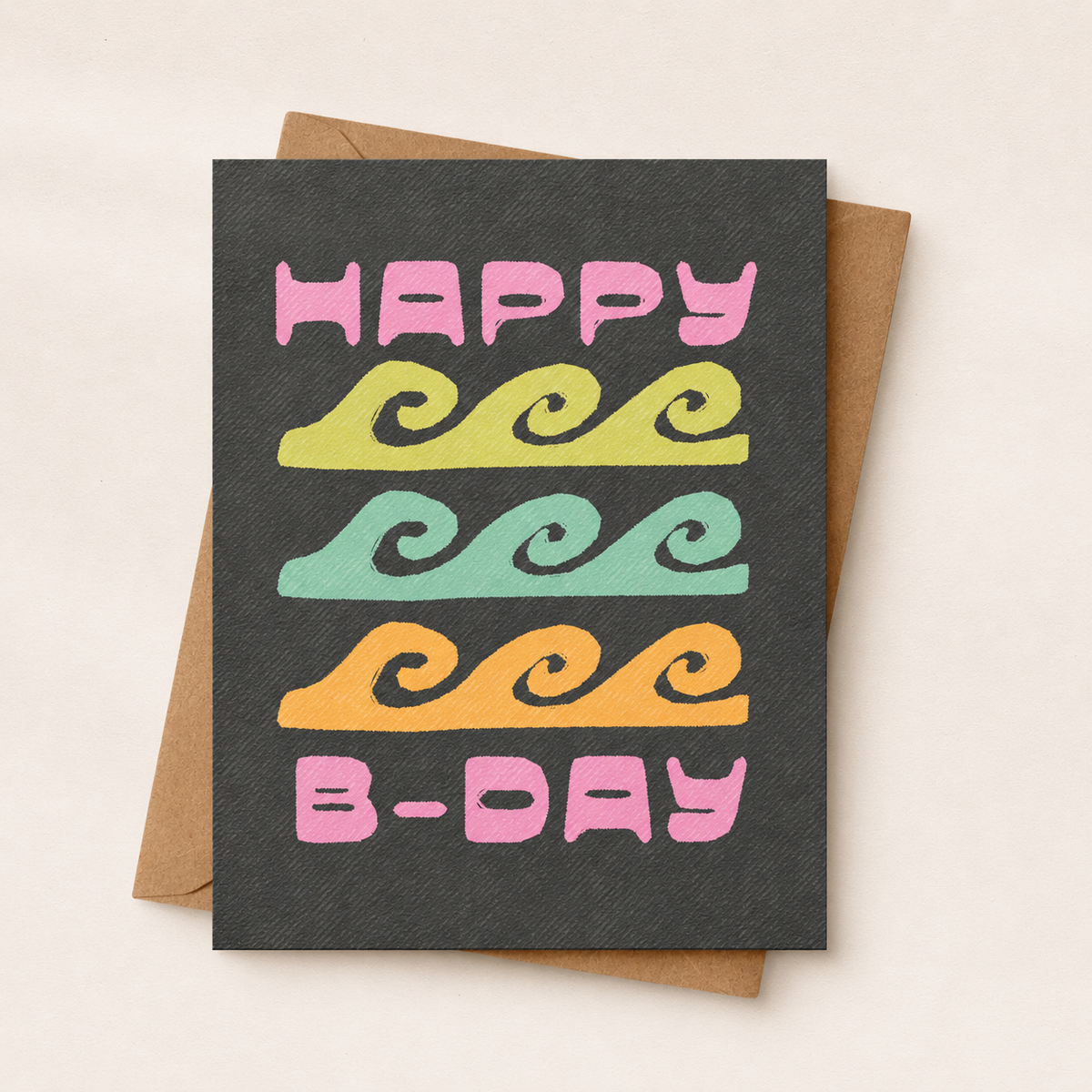 A square birthday card with a dark charcoal textured background and the words “HAPPY B-DAY” in pink, yellow, mint green, and orange wavy lines, shown with a brown envelope on a light beige background.