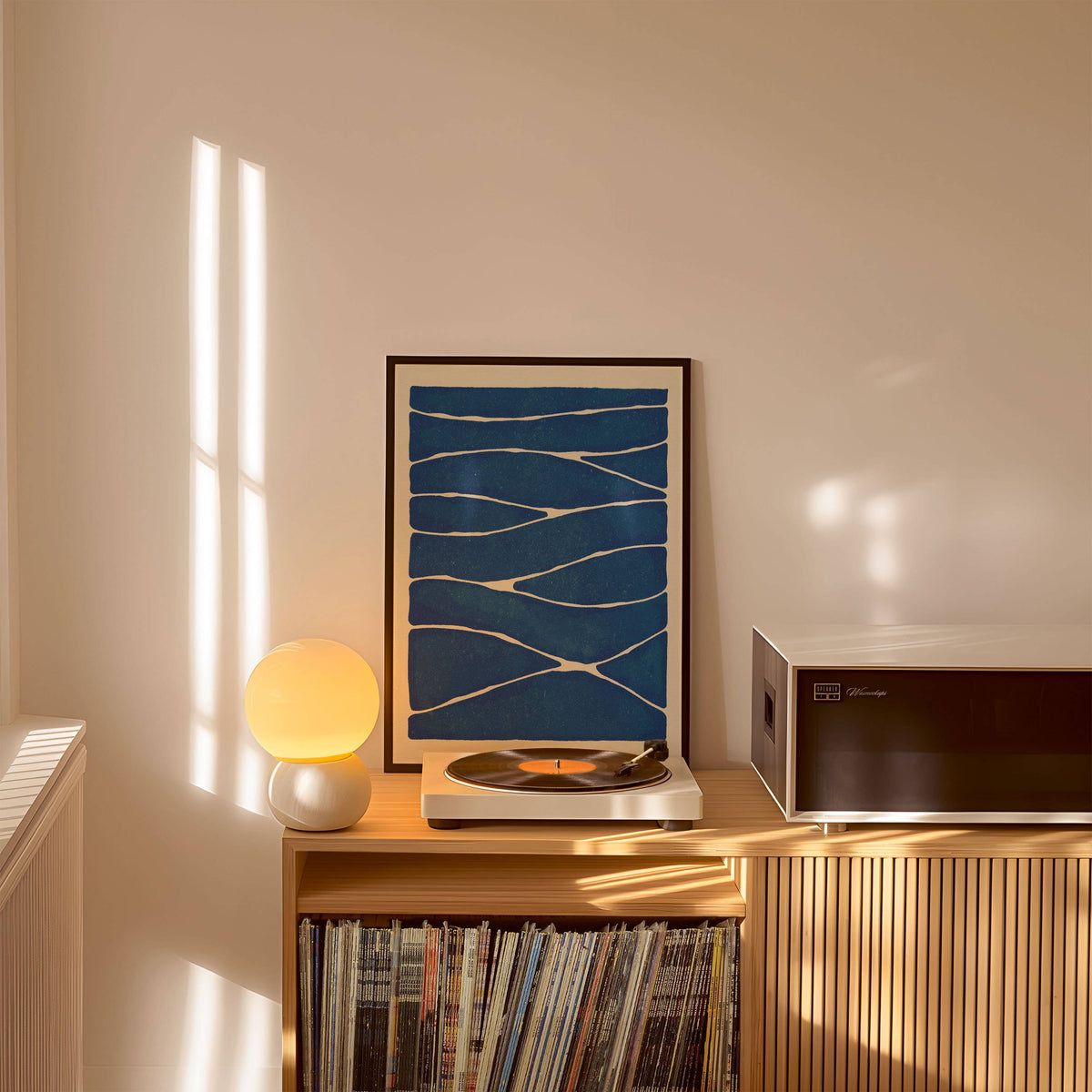 Turntable with vinyl records on a wooden cabinet, framed artwork, and lamp in a room.