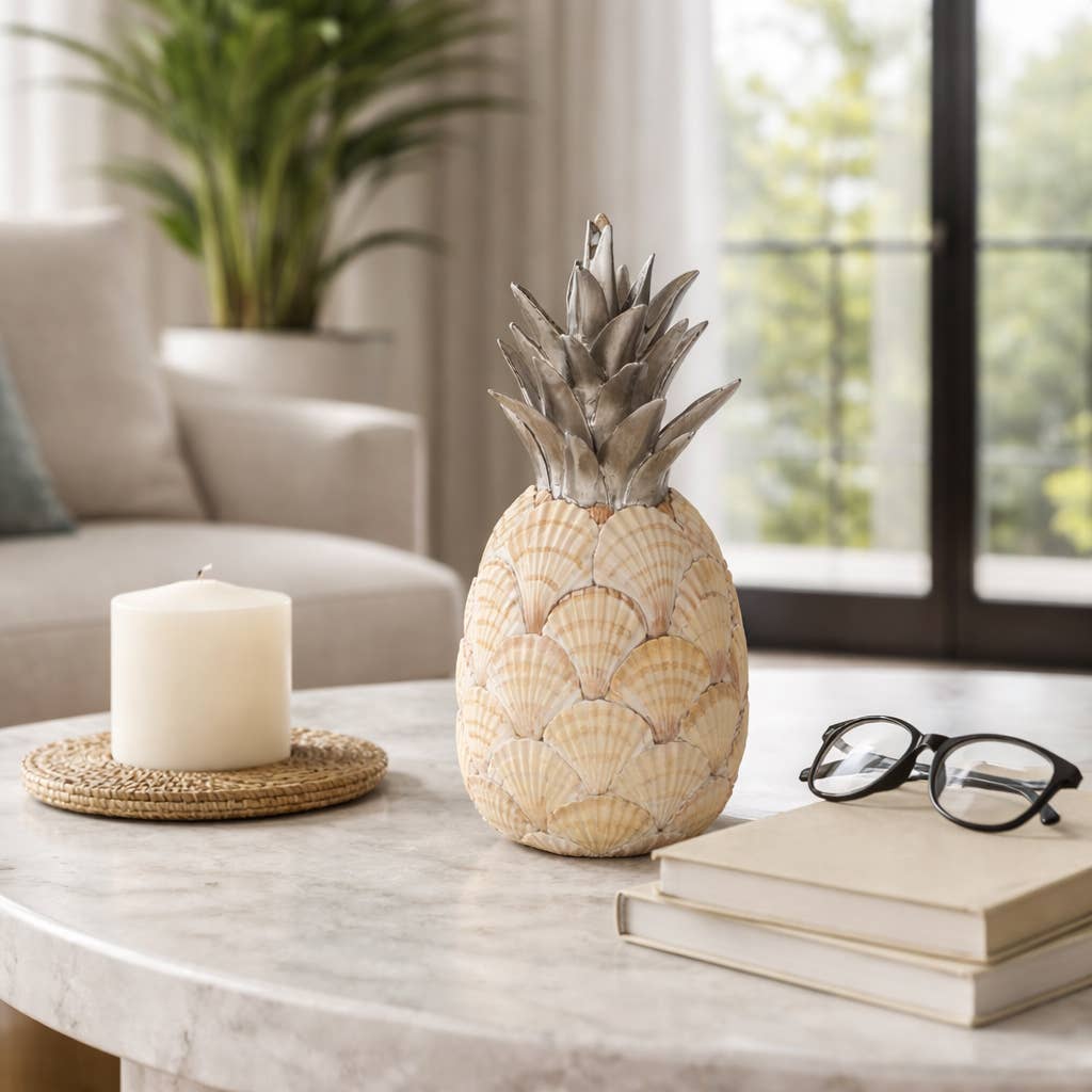Decorative pineapple made of seashells on a marble table with books and a candle.