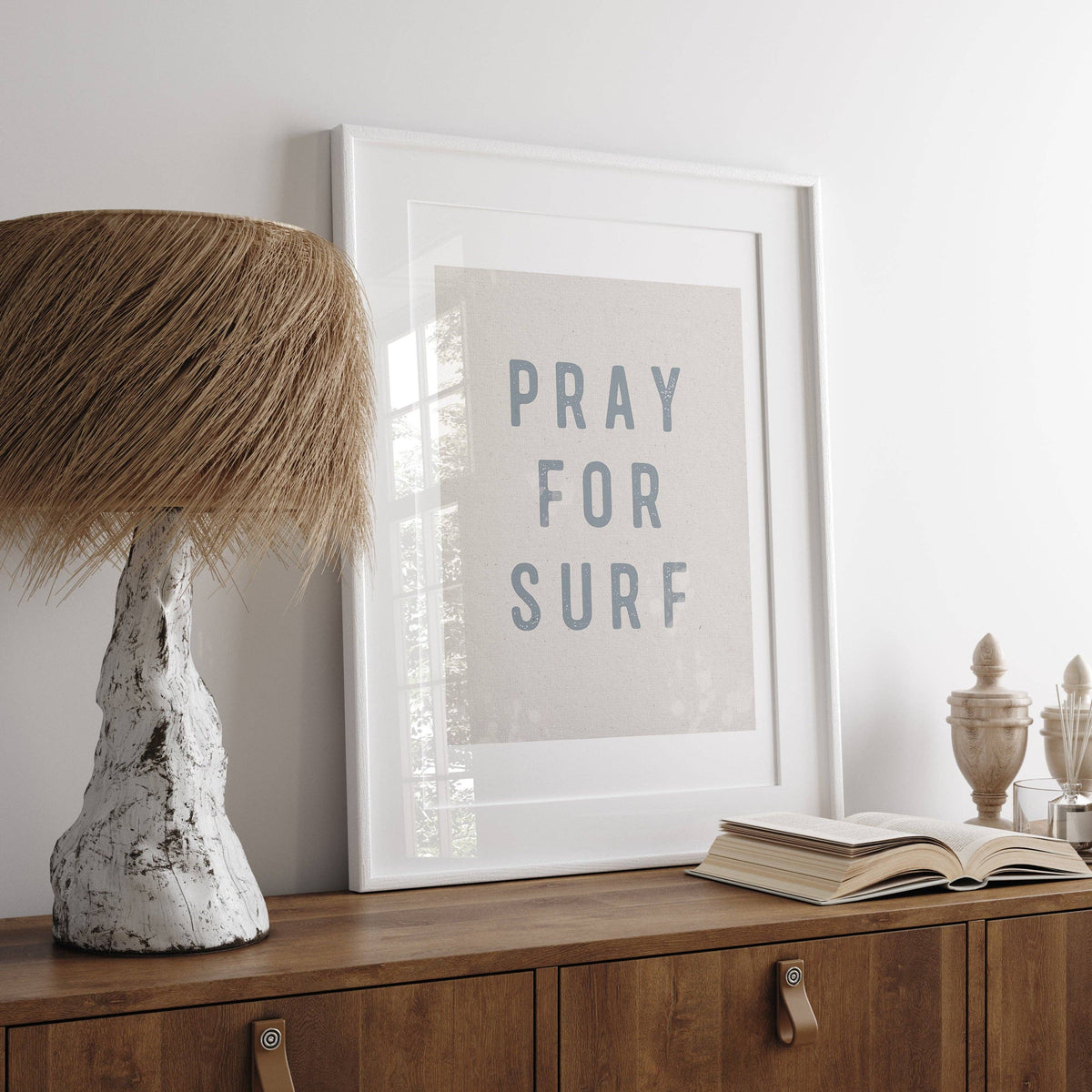 Framed artwork with 'PRAY FOR SURF' text on a wooden surface with decorative items.