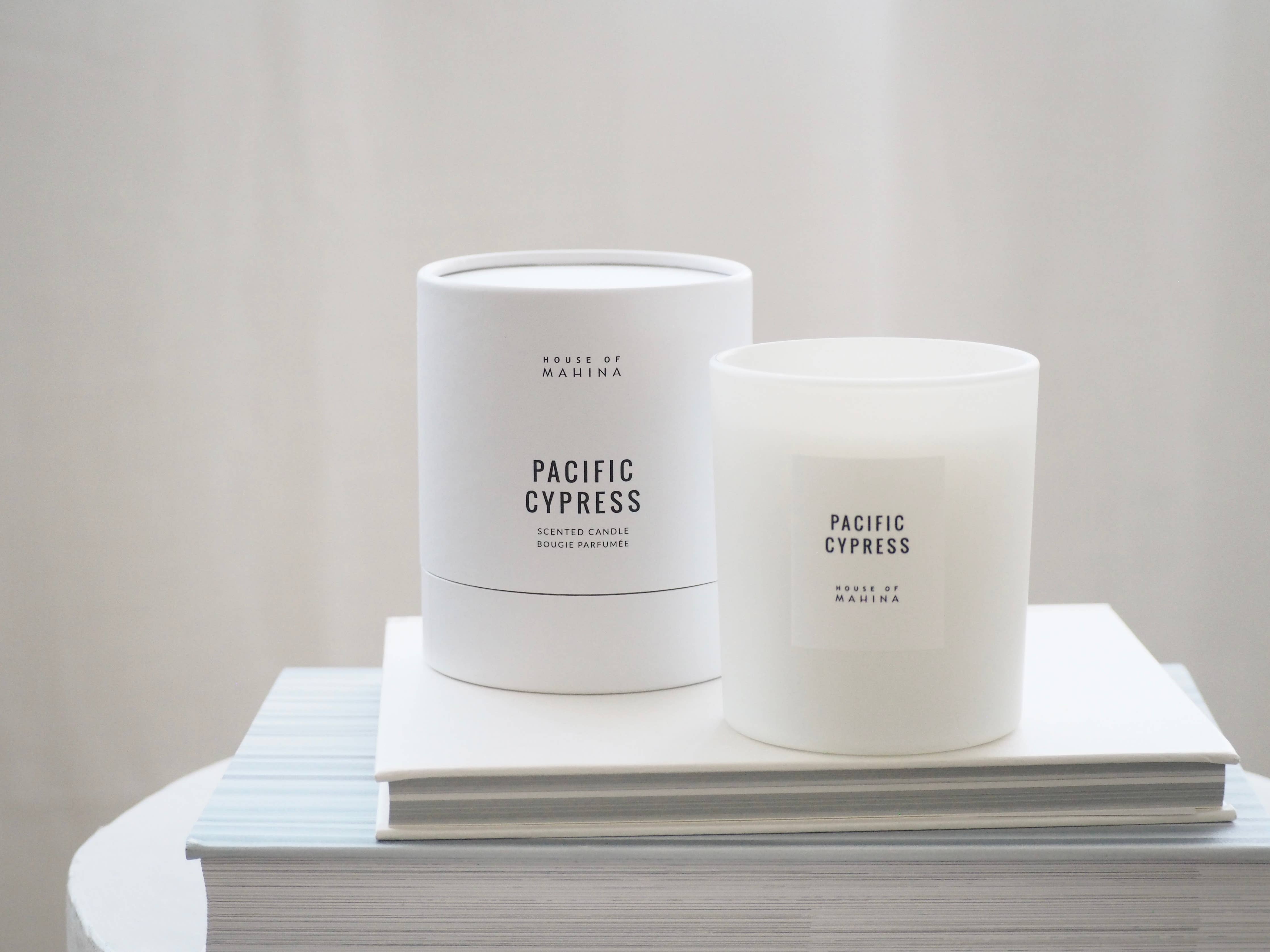 Two 'Pacific Cypress' candles on a stack of books with a plain background