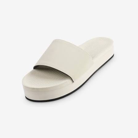A single platform slide sandal in a light cream or off-white color, shown from a three-quarters angle against a plain white background.