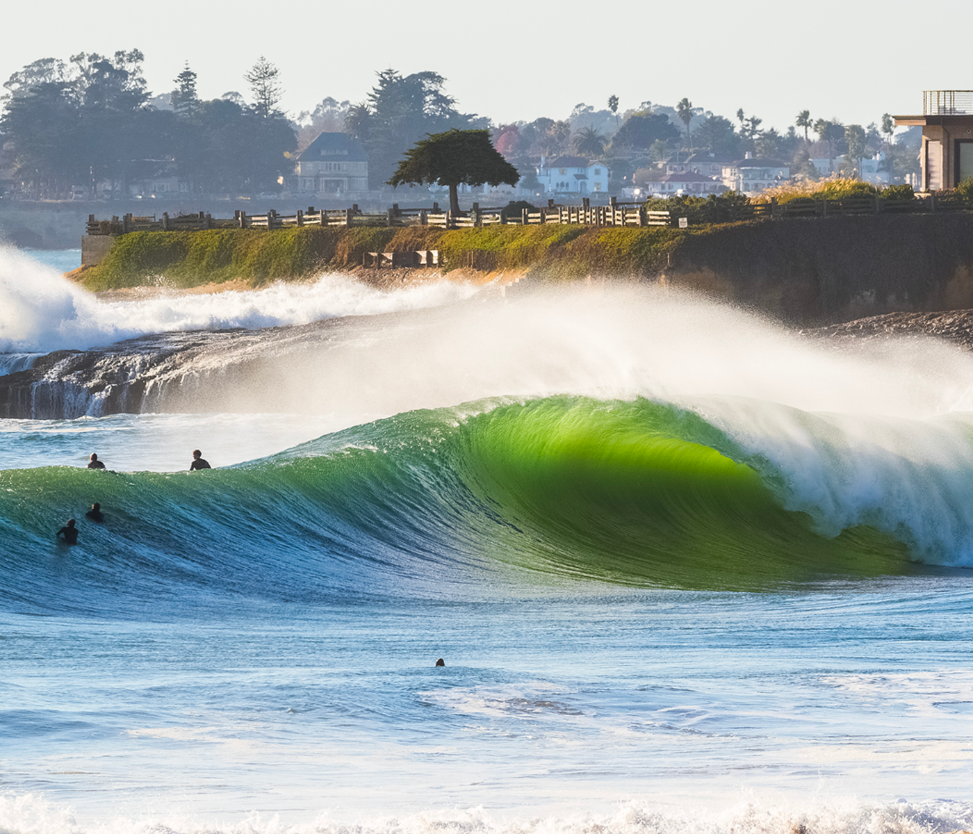 A large wave in the ocean with a coastal town in the background.
