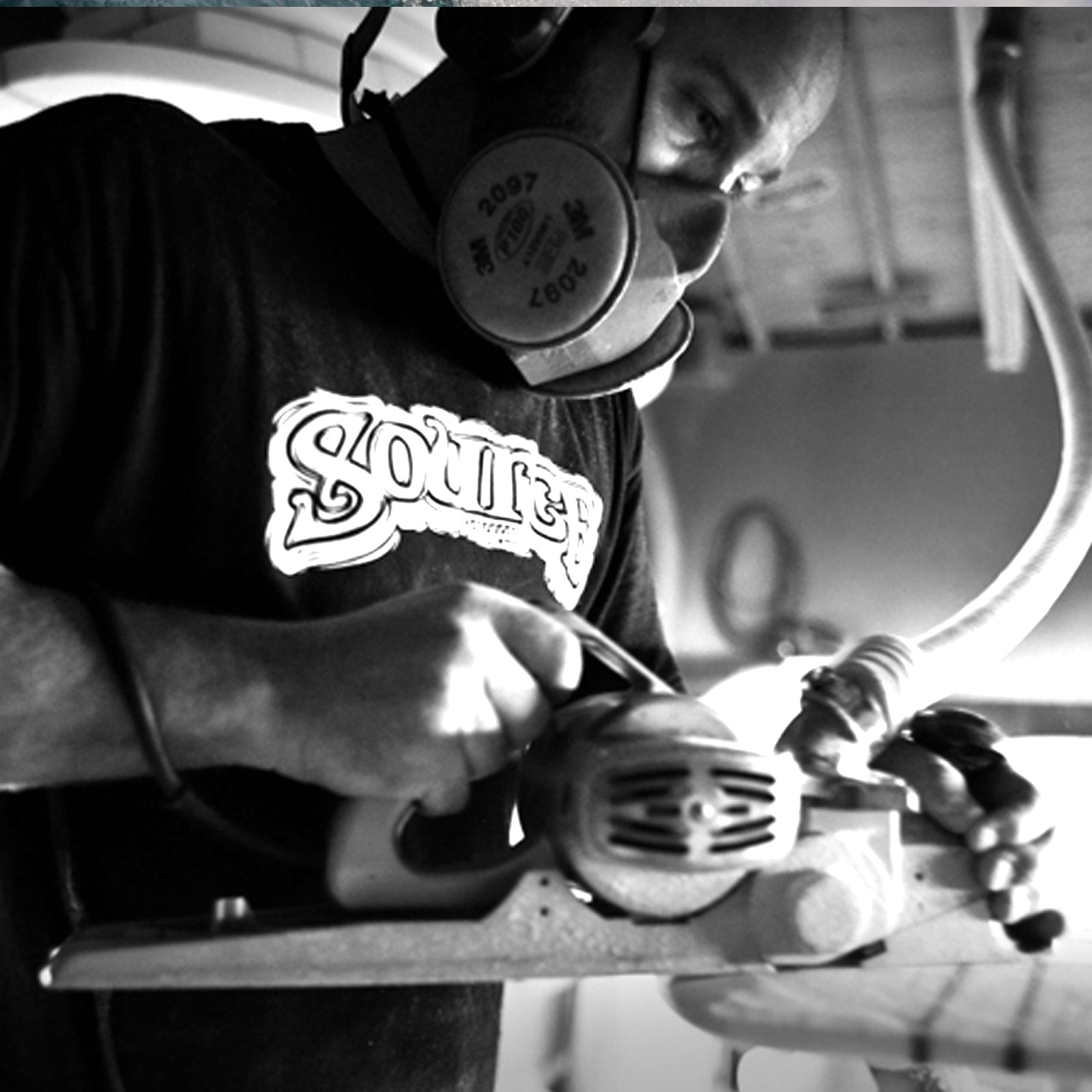 Person shaping a surfboard with a hand planer at Source Surfboards