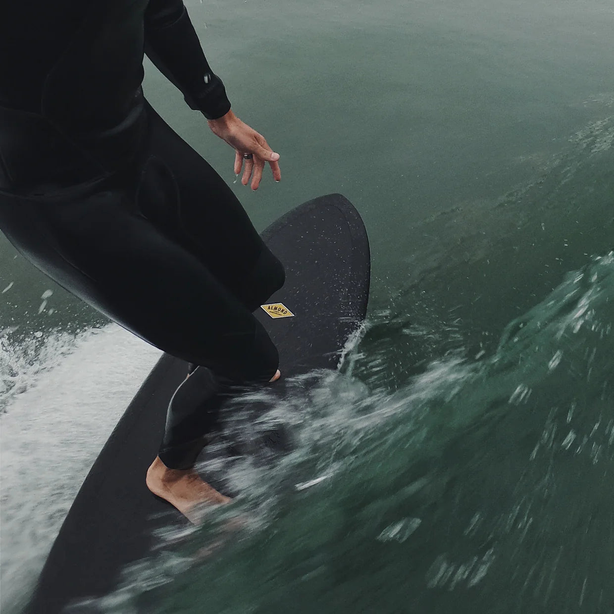 Person surfing on a wave wearing a black wetsuit and riding an Almond surfboard