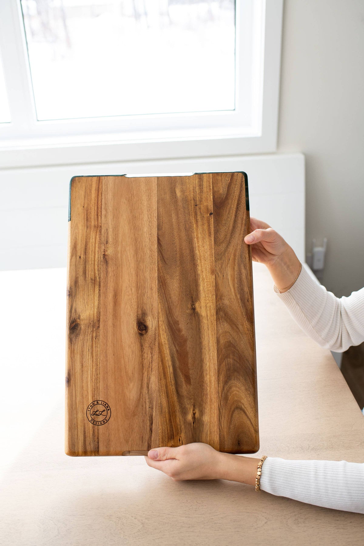 Person holding a wooden cutting board with a visible brand logo.