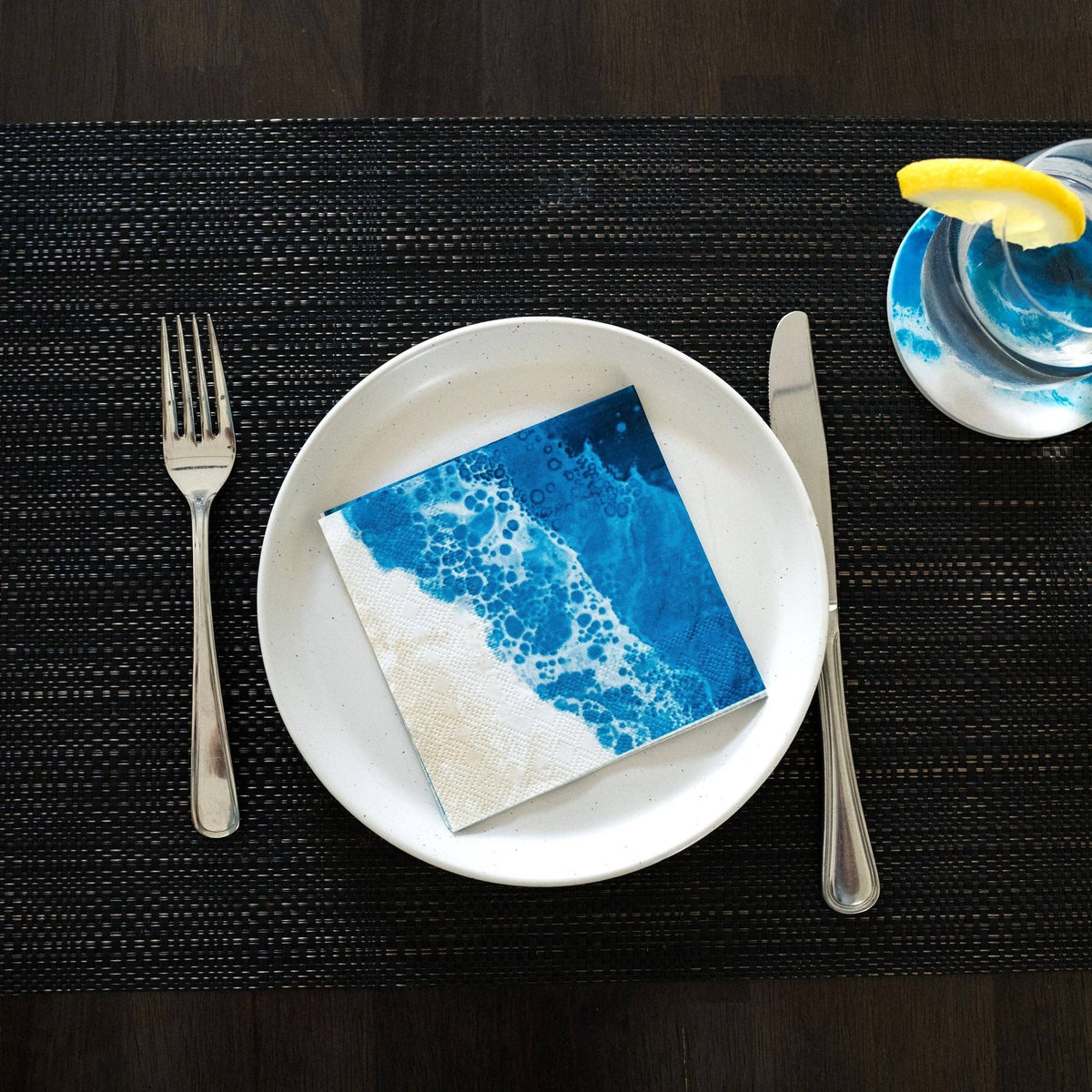Napkin with ocean wave design on a white plate with cutlery, on a dark placemat.