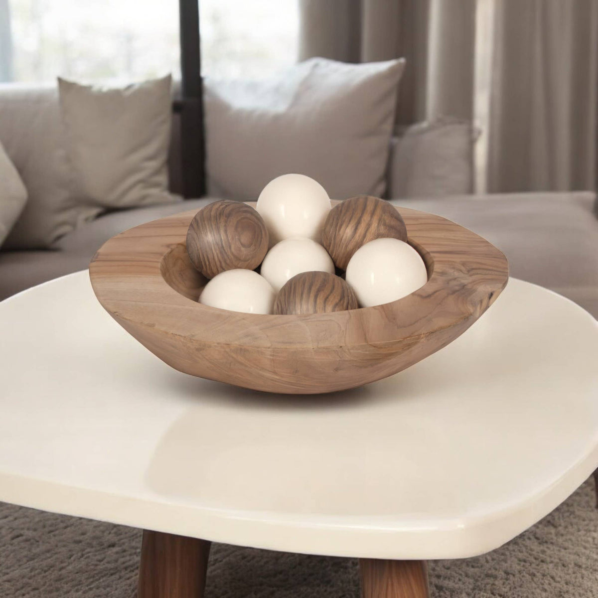 Wooden bowl with spherical objects on a white coffee table in a living room setting.