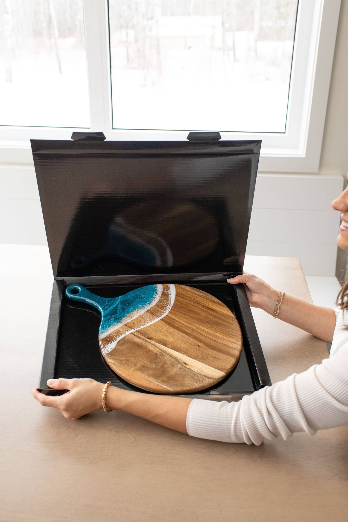 Person holding a black box containing a wooden cutting board with a blue handle.