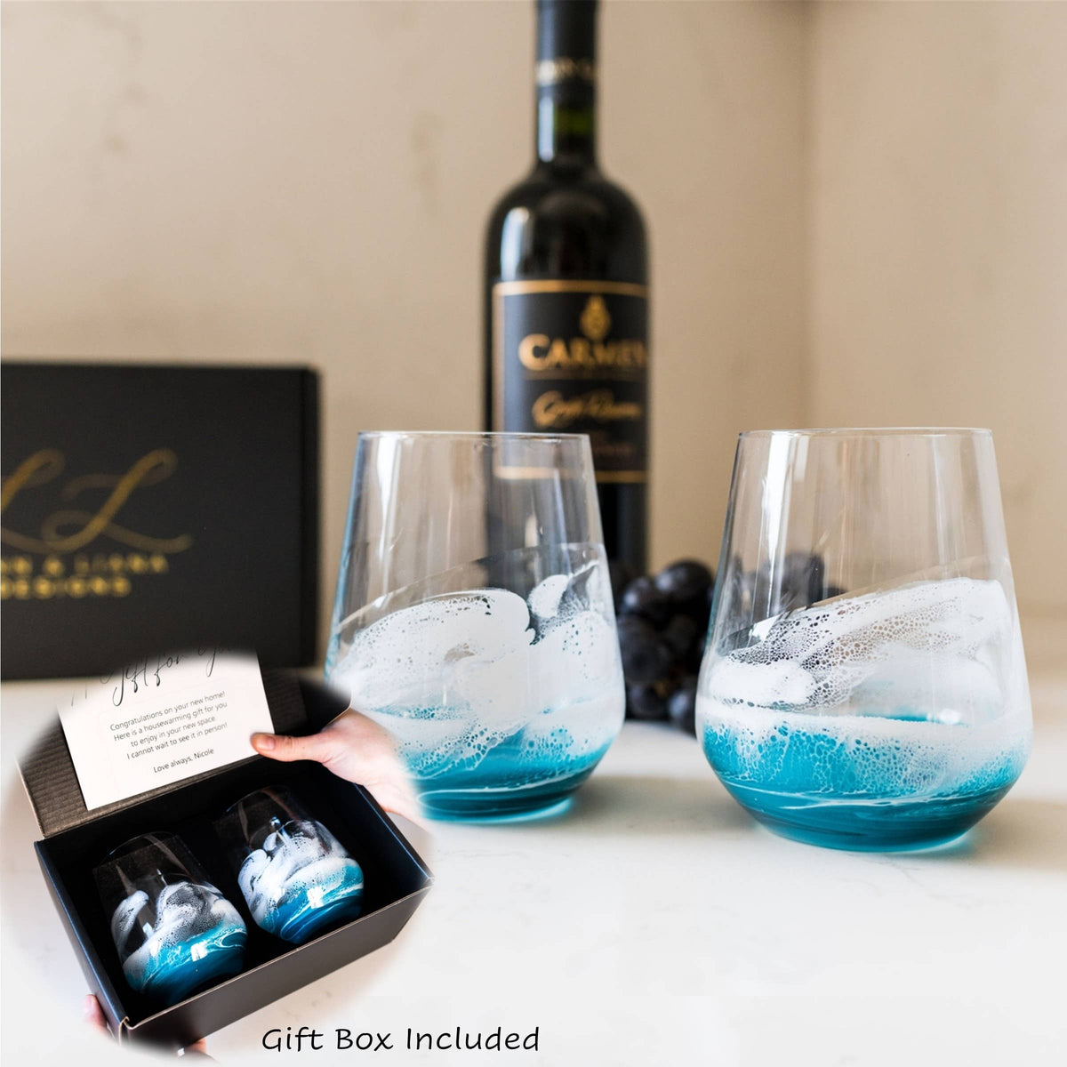 Two wine glasses with blue and white design, a bottle of wine, and a gift box on a table.