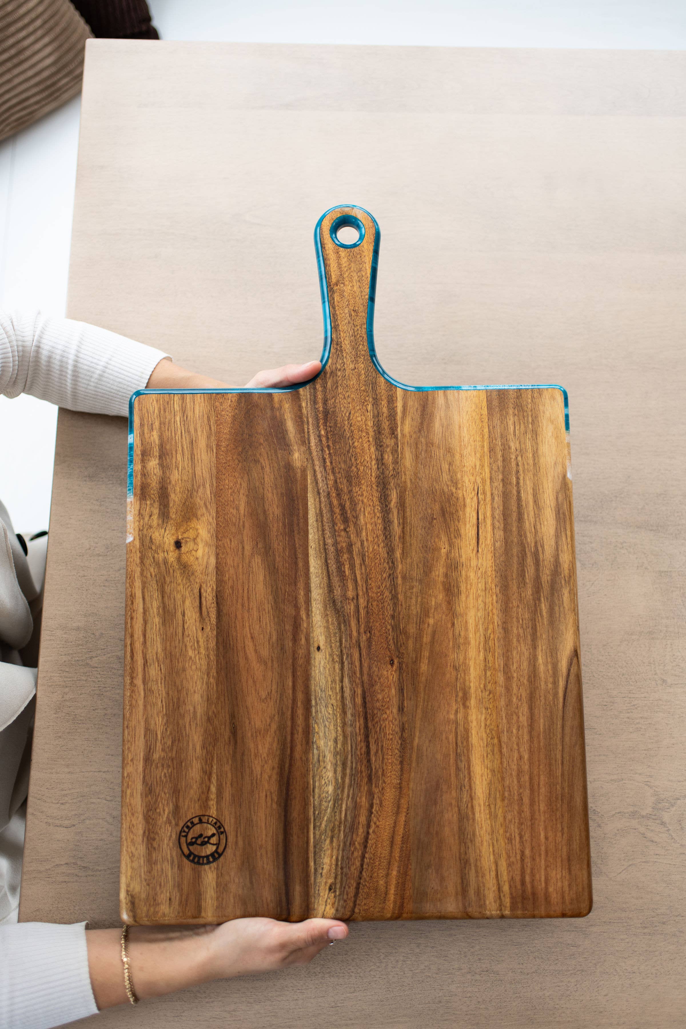 Wooden cutting board with a handle held by a person on a beige surface