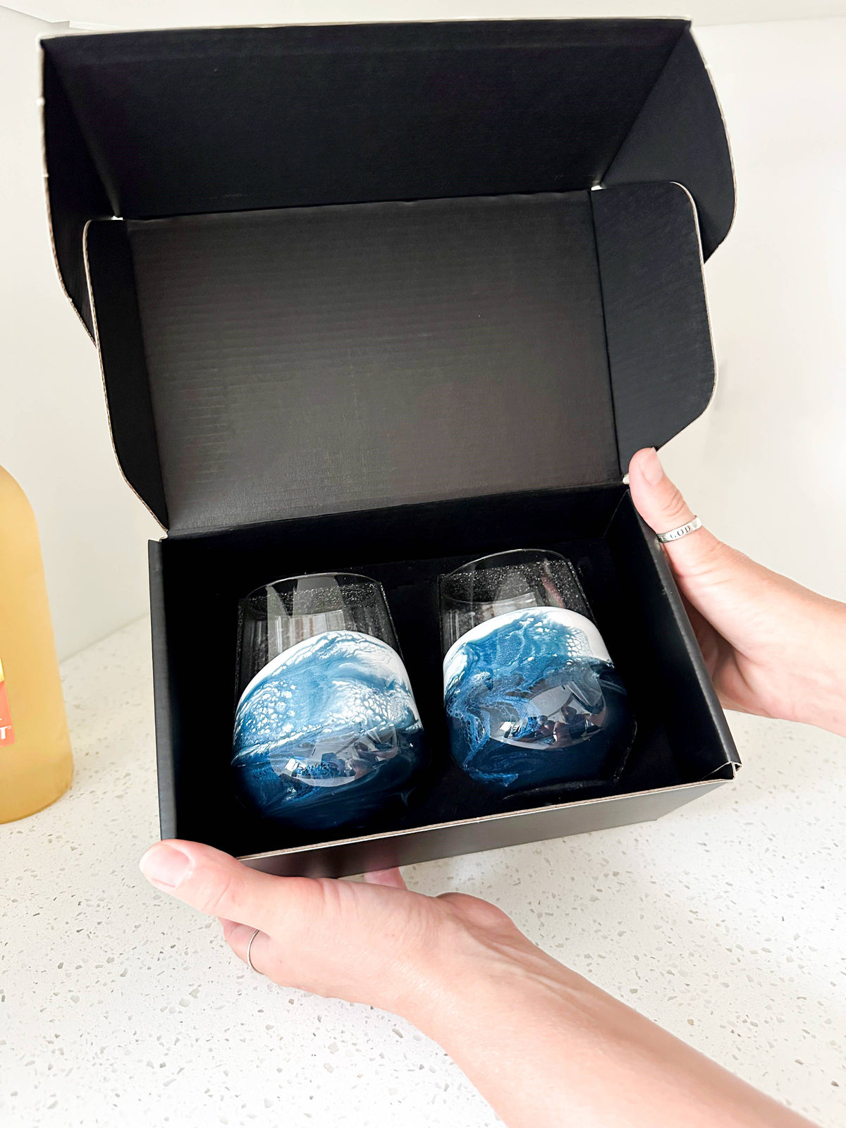 Two blue glass tumblers in a black box held by a person.