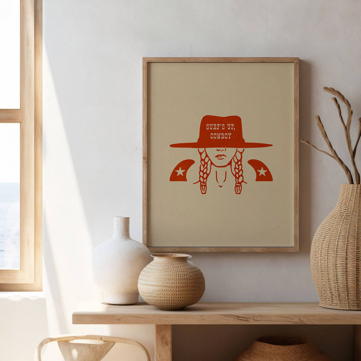 Framed artwork of a person wearing a hat with text, displayed on a wall above a wooden shelf with decorative vases.
