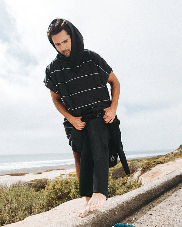 Man in a Black Sand Cloud Border Classic Stripe Poncho with ocean and sky in the background.