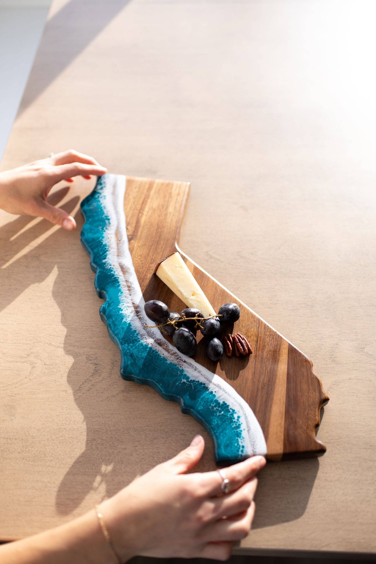 Wooden cutting board with blue resin design held by a person on a light wooden surface.