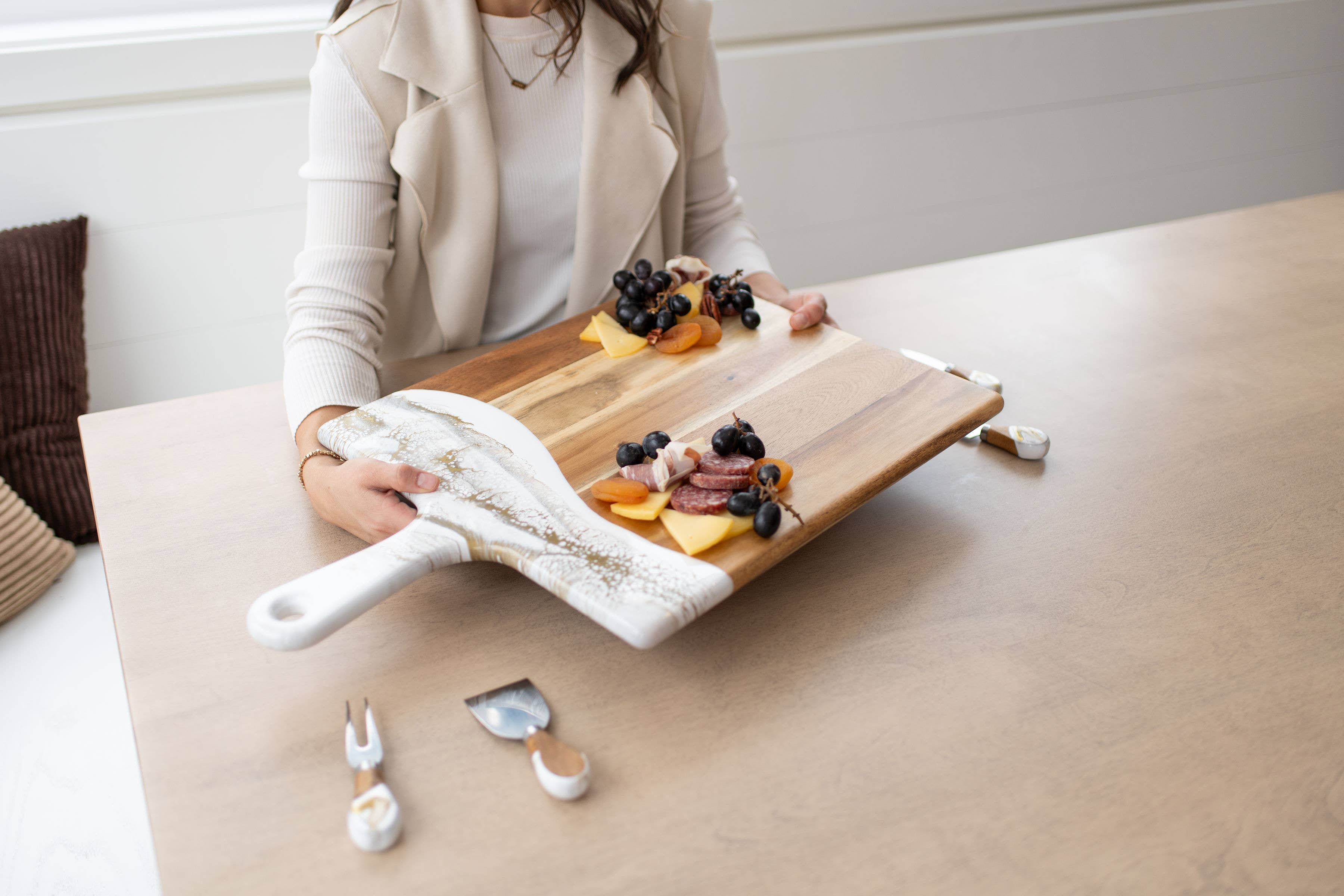 Person holding a cheeseboard with various foods on a table