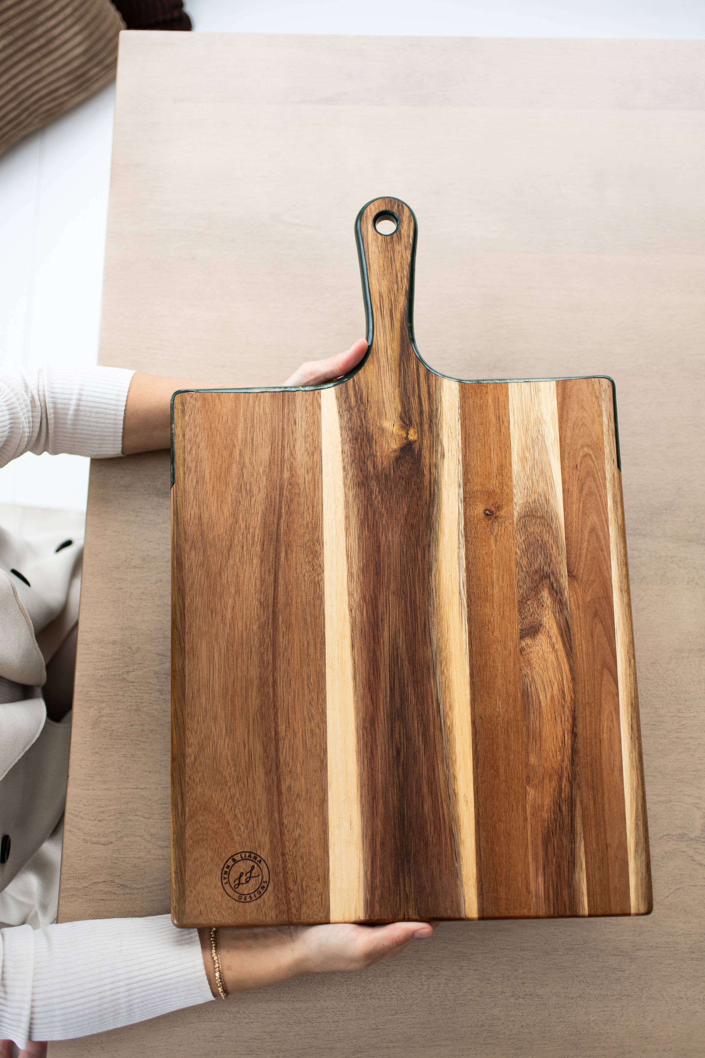 Wooden cutting board with a handle held by a person on a neutral background
