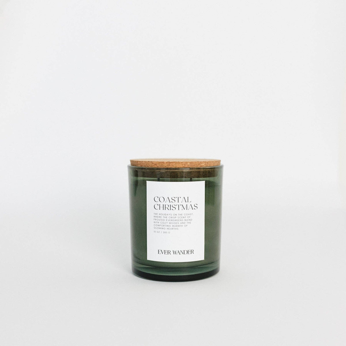 A dark green glass jar candle with a natural cork lid and a white label reading 'COASTAL CHRISTMAS' and 'EVER WANDER', centered on a clean white background.