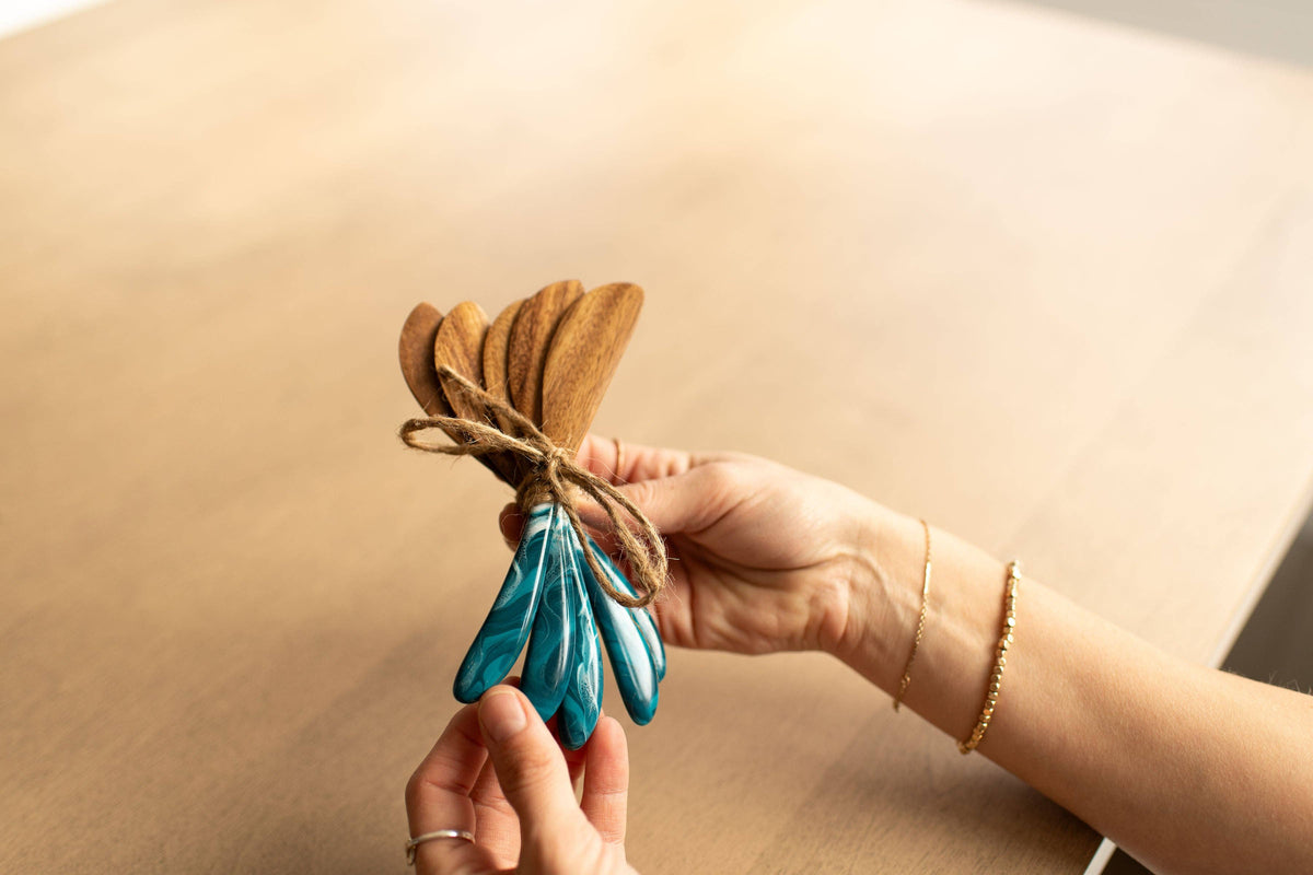 Hand holding a bundle of wooden and blue ceramic fans against a beige background