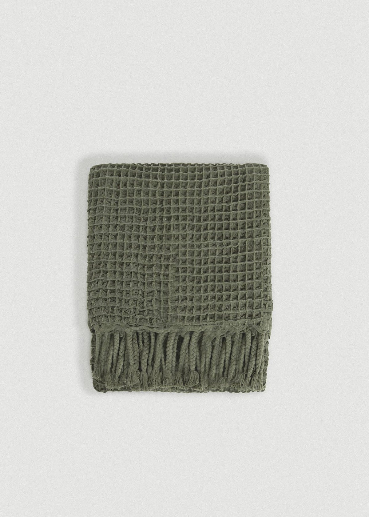 An olive green waffle-knit scarf with fringed edges, laid flat against a light gray background.