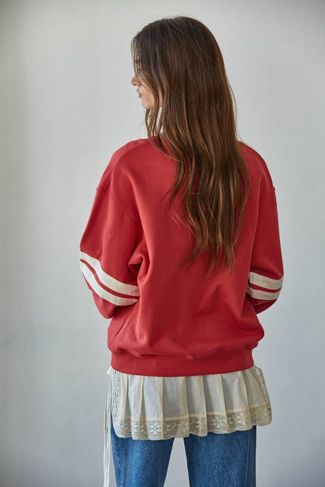Person wearing a red sweatshirt with white stripes on the sleeves, standing against a plain background.