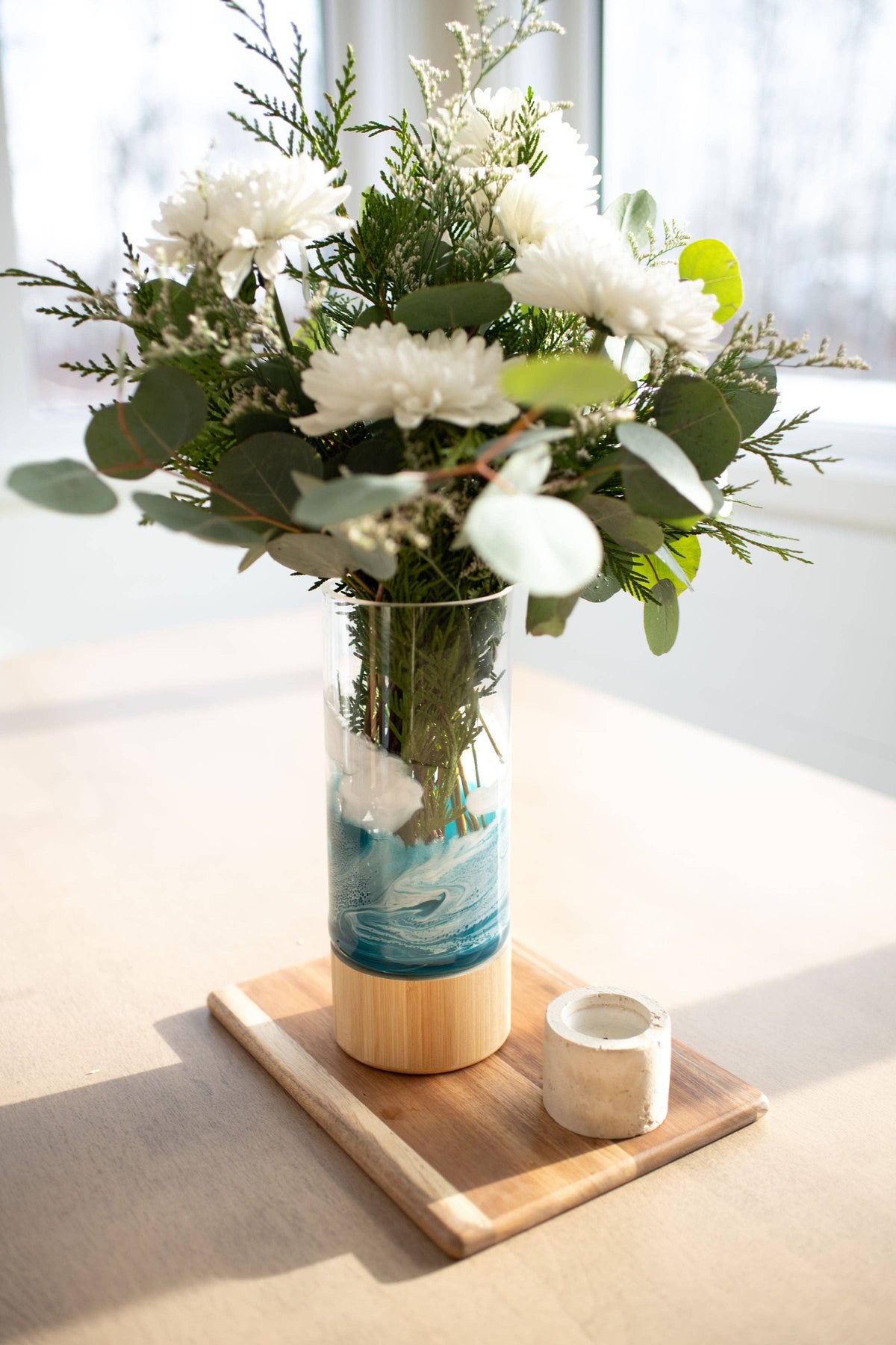 Floral arrangement in a vase on a wooden tray with a white background